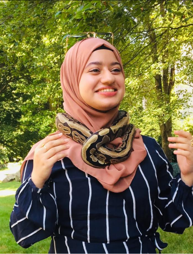 Portrait shot of Maha Alam wearing a pink hijab and blue and white stripped shirt with snake wrapped around her neck