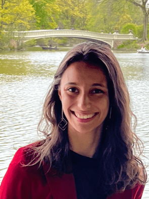 Medium close up shot of Sarah Johnson by a lake with medium length wavy hair and a red shirt