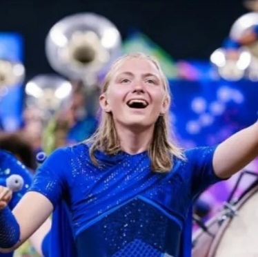 Medium close-up shot of Valen Fisher with blonde half-tied back hair and wearing a blue shirt performing at his band