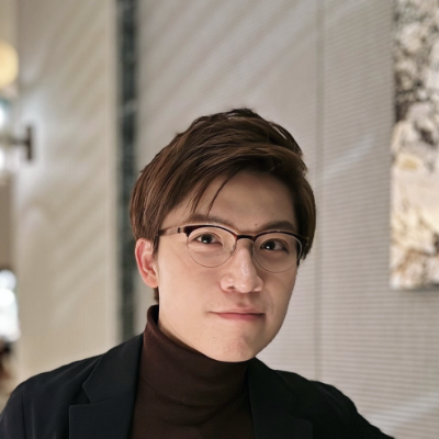Headshot of David Wei Dai Wearing Black Suit and Burgundy Sweatshirt Against Bright Background