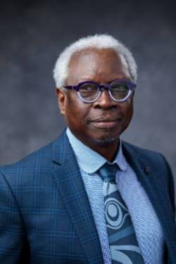 Headshot of Salikoko Mufwene in Dark Navy Suit Against Dark Grey Background