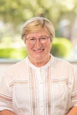 Headshot of Angela Scarino Wearing a White Mid-Sleeved Shirt Against a Nature Background