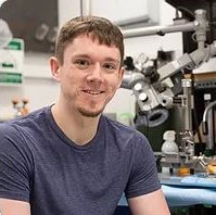 Headshot of Liam Lang in front of a microscope