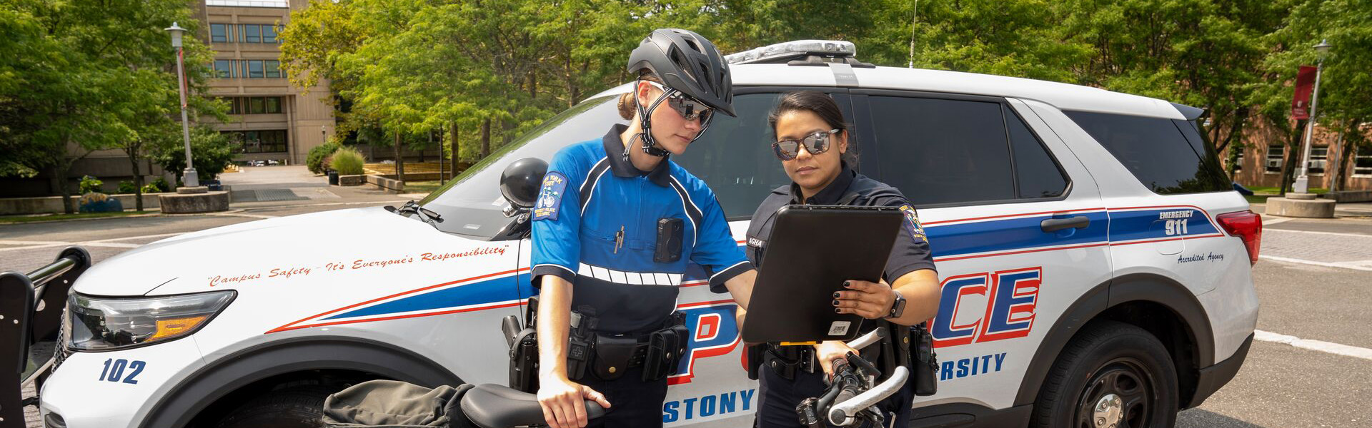 Police Officers looking at a tablet in front of a police cruiser