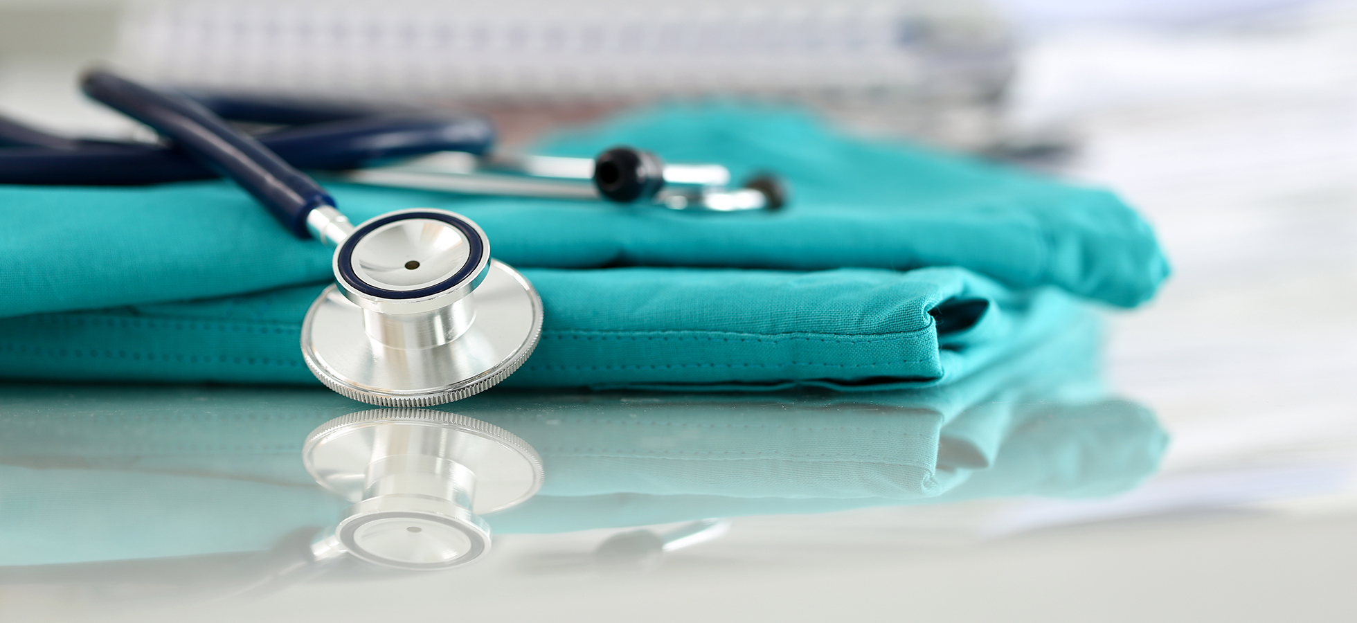 Stethoscope on folded teal medical scrubs.