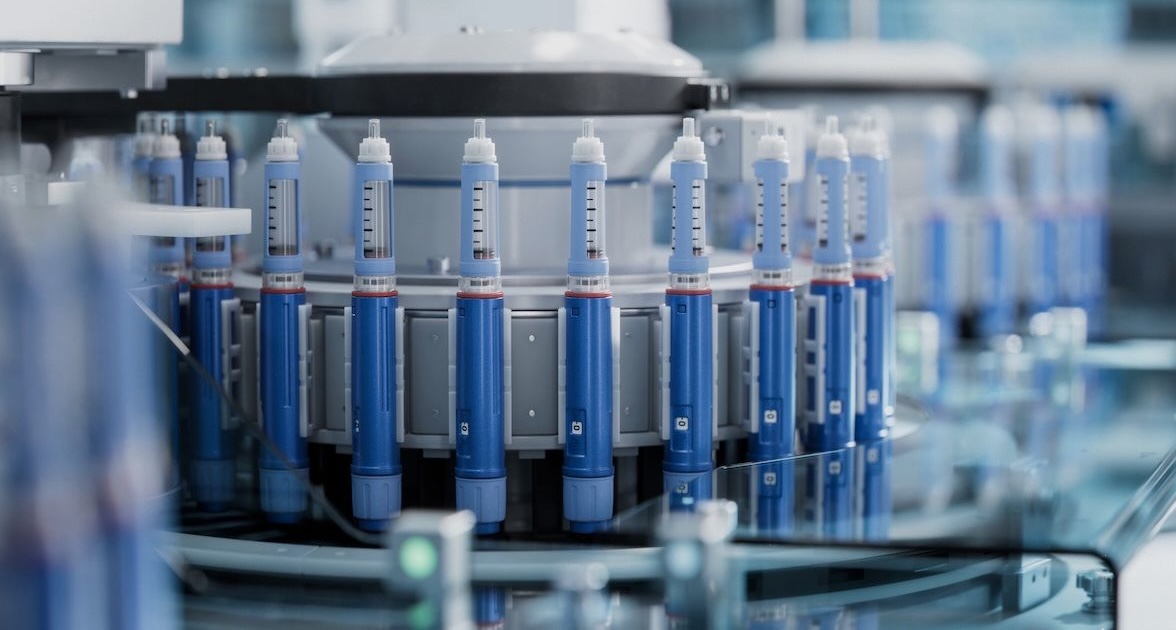 Automated machinery assembly line processing blue medical injector pens or syringes.
