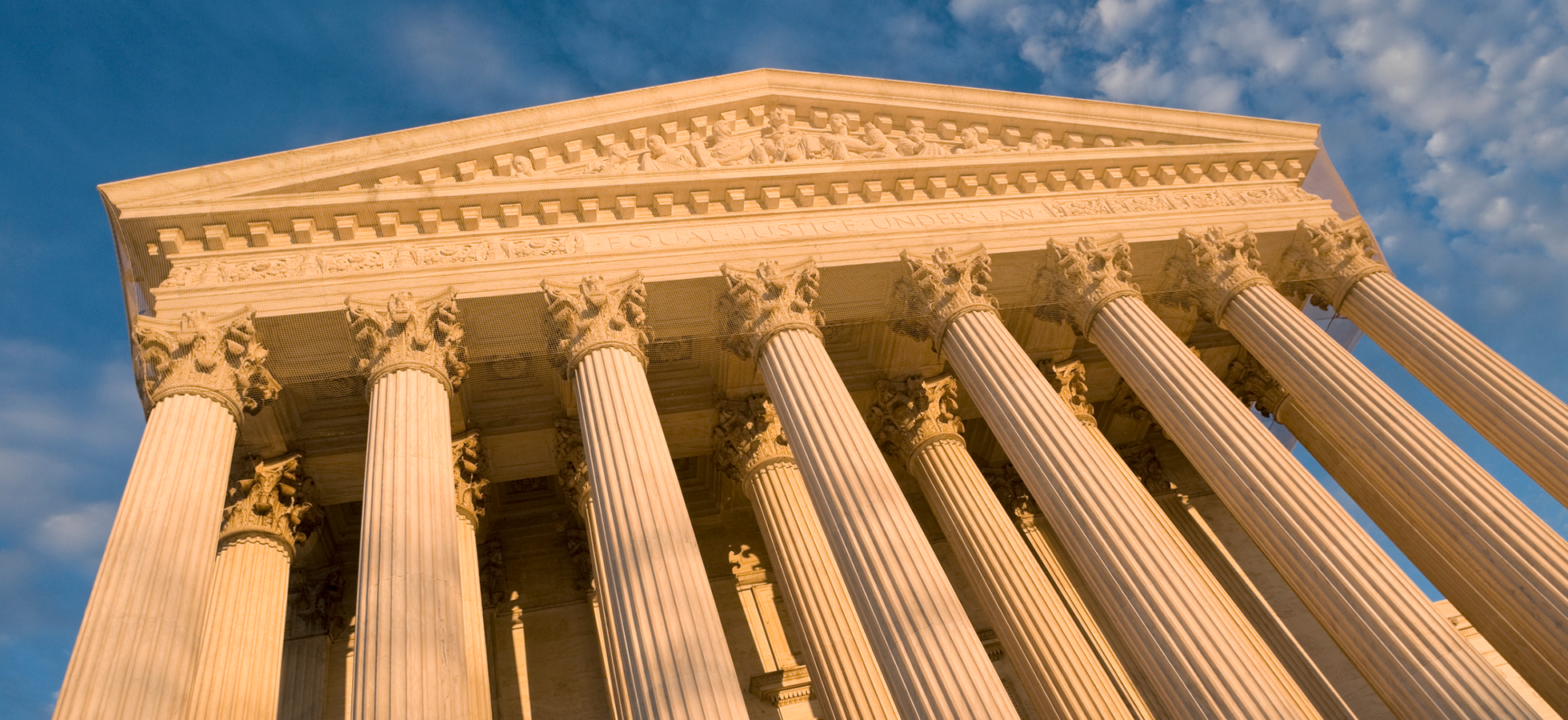 A low-angle view of the marble Corinthian columns and architectural details of a classical court building facade under a blue sky.