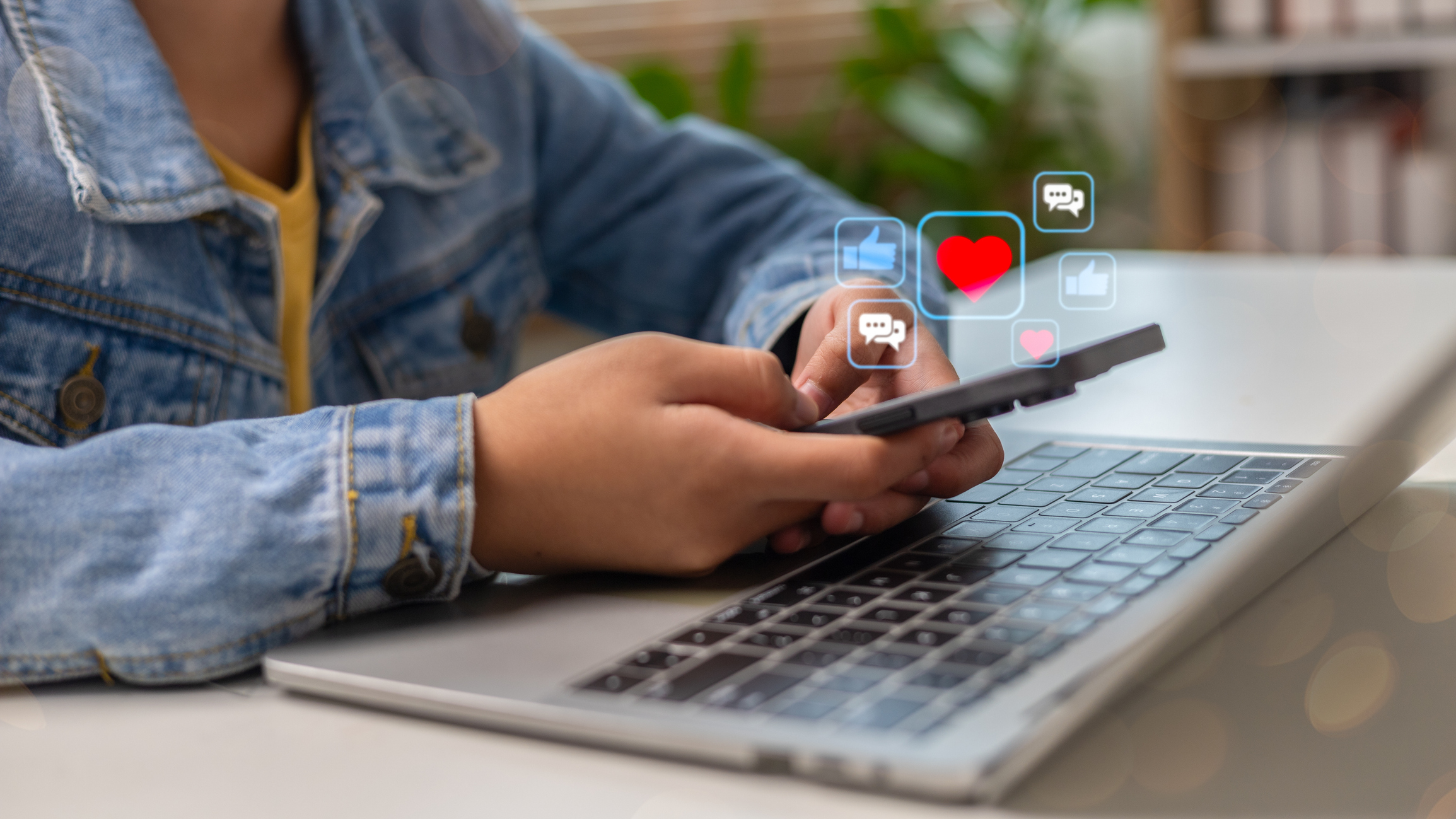 Person using a smartphone over a laptop with social media icons.