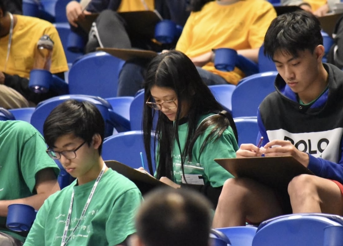 Students sitting in stadium seating and writing on clipboards.