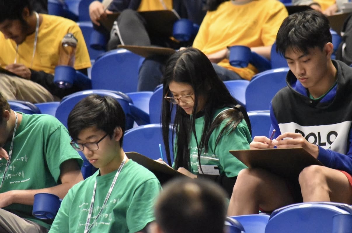 Students sitting in stadium seating and writing on clipboards.