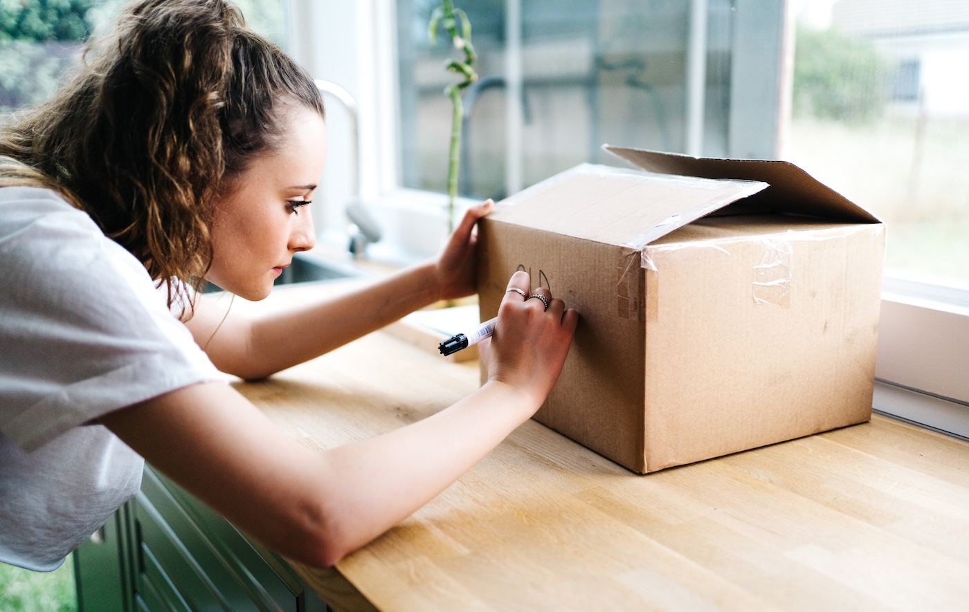 A person writing on a cardboard shipping box with a black marker on a wooden counter.