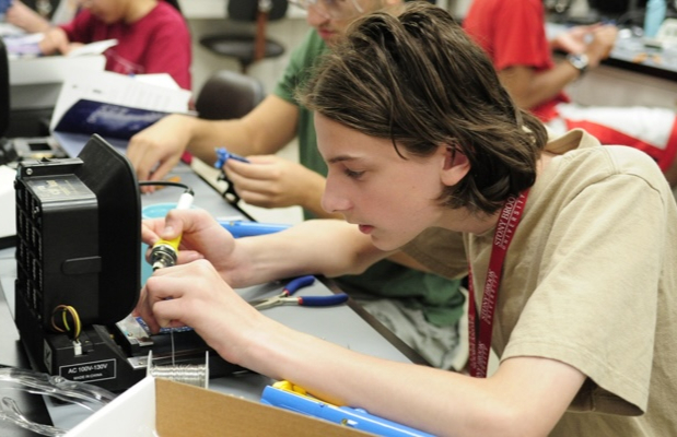 A student uses a soldering iron to work on a circuit board at a laboratory workbench.