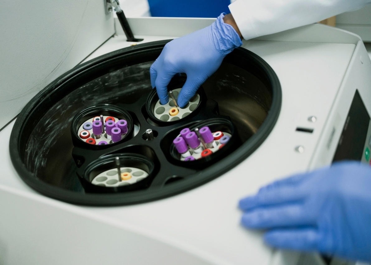 A gloved hand placing a vial of liquid into a centrifuge