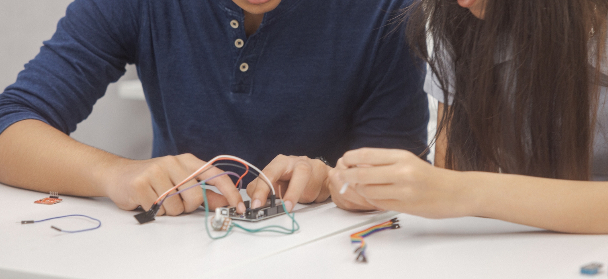 Two people working together to connect wires to an electronic component on a desk.