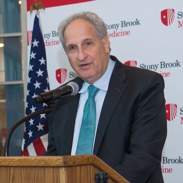 Ben Luft speaks at a podium in front of an American flag and a Stony Brook Medicine backdrop
