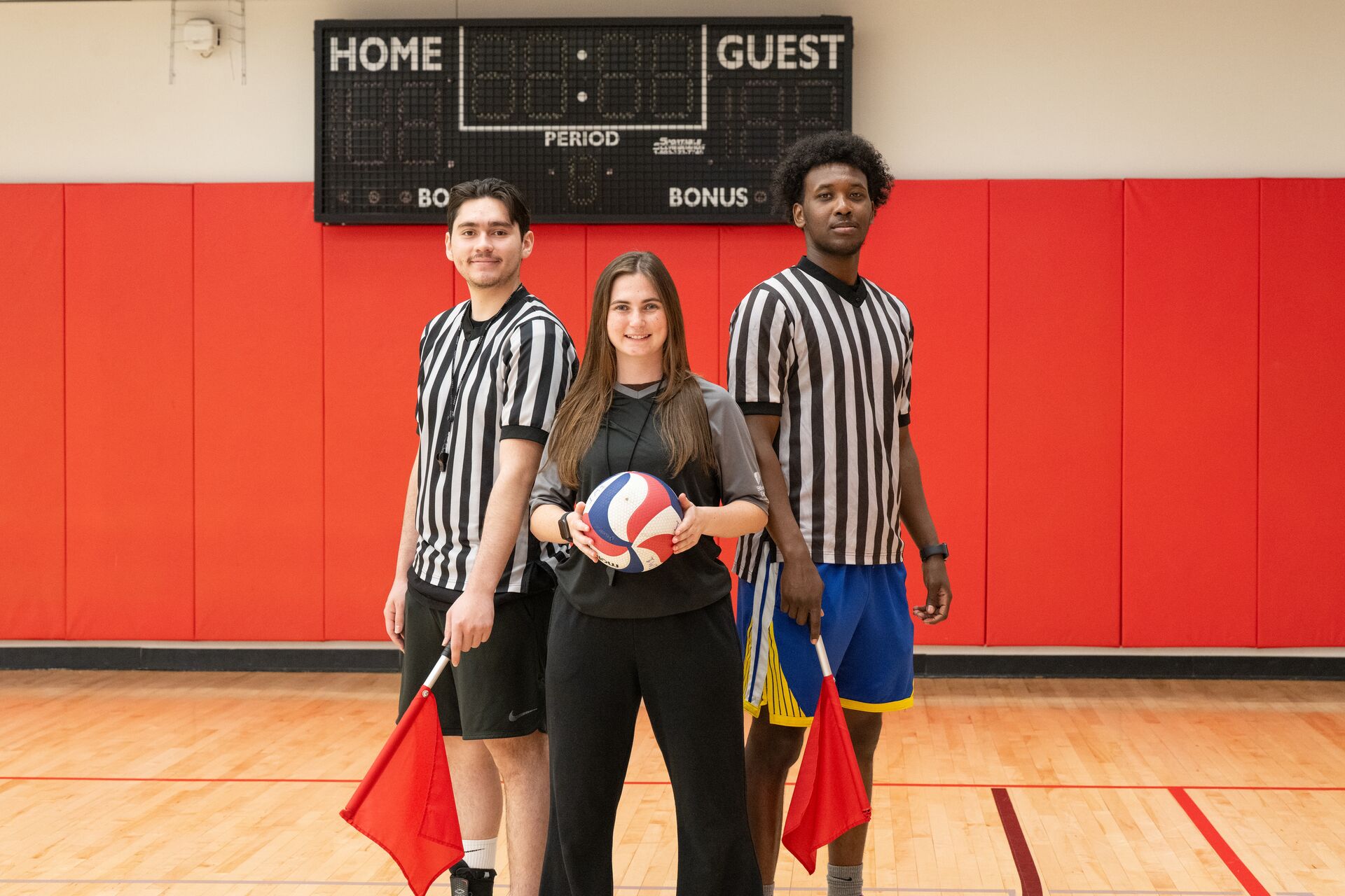 Two referees and a volleyball player standing next to each other on a gym court.