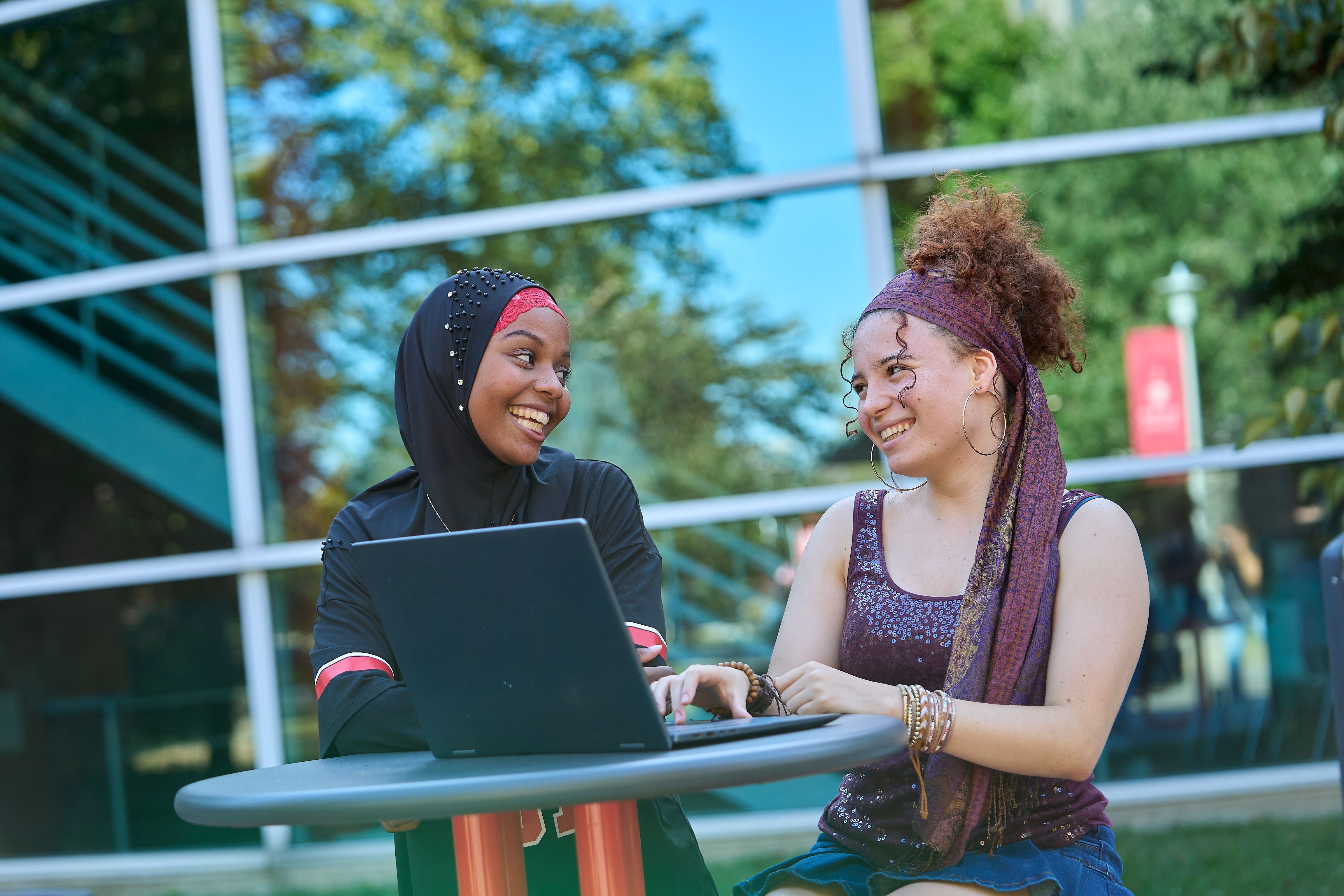 two students sitting outside using a laptop