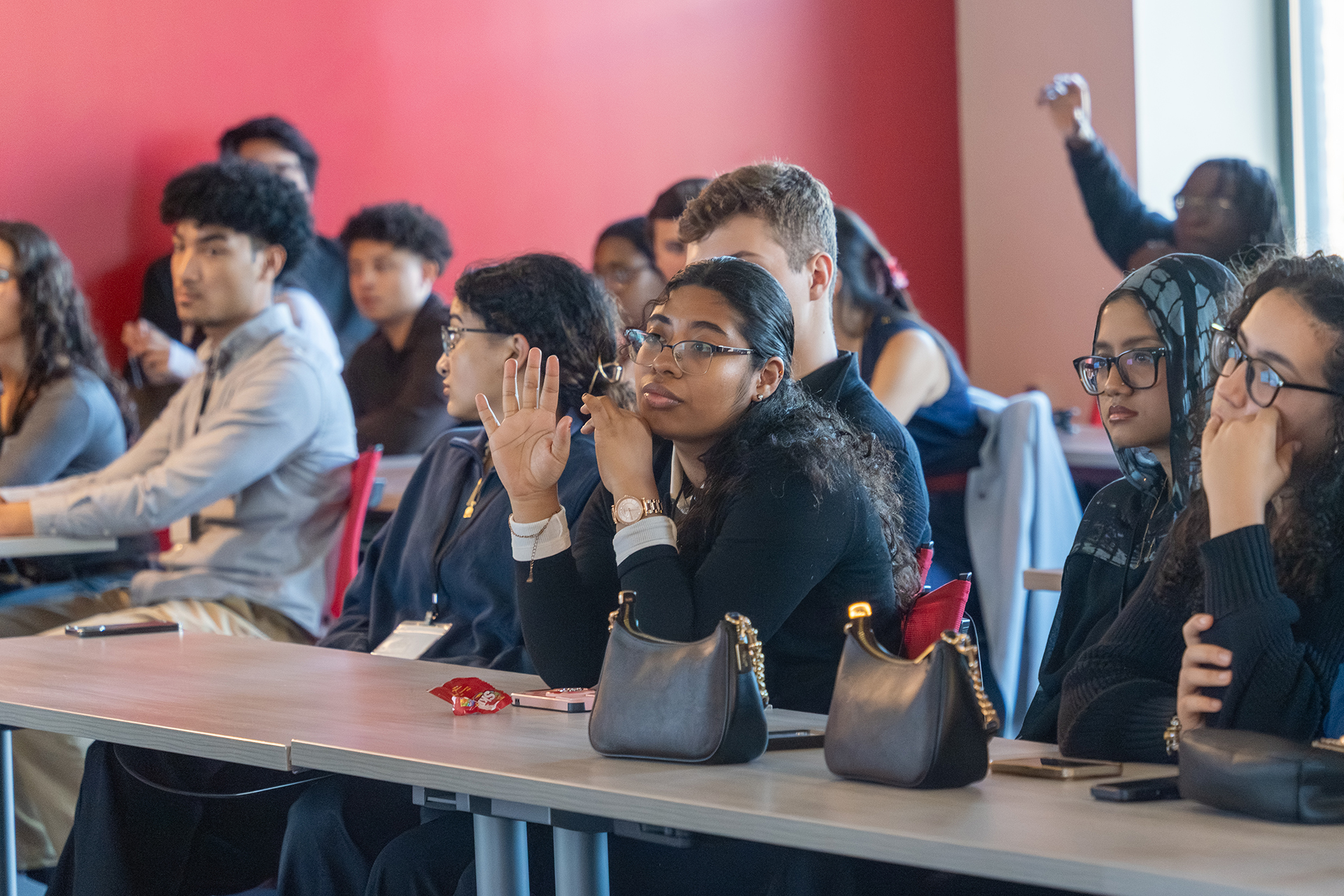 Two students raising their hands in a full classroom.