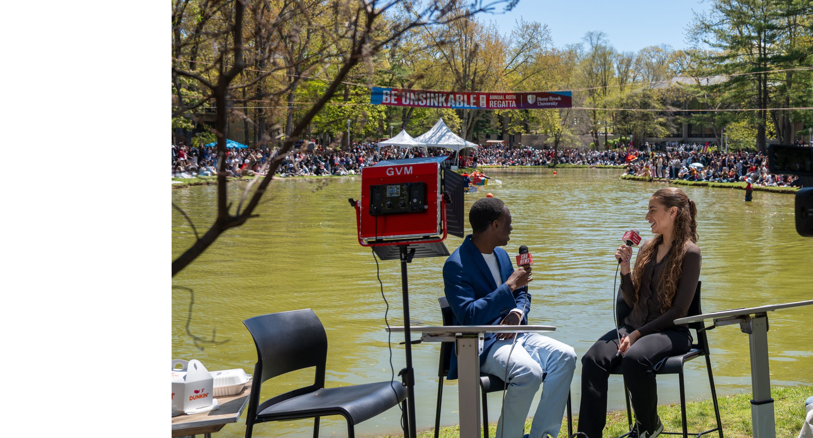 Two students hosting a live news broadcast in front of Roth Pond on Stony Brook University's campus.