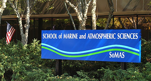 The sign for the School of Marine and Atmospheric Sciences sits among the trees with a US flag in the background