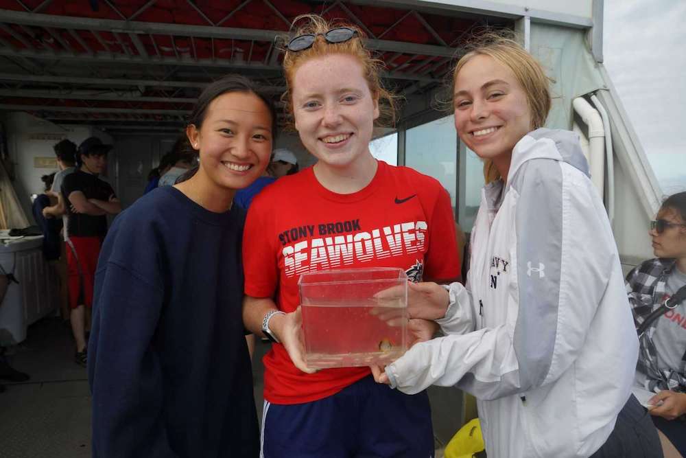 Three students look at the camera while showing off what they caught in the net
