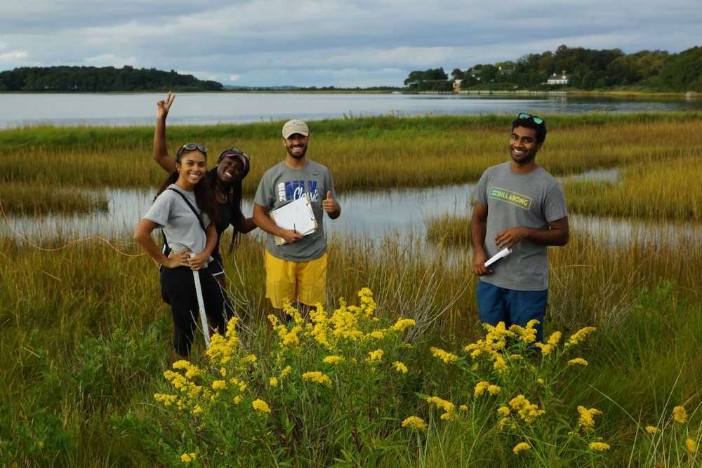 A group of students smile at the camera whil standing in the marsh conducting field work