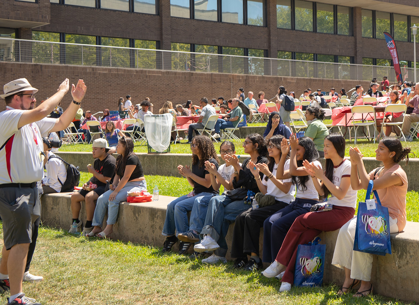 Students sitting outdoors clapping and smiling at a campus event.