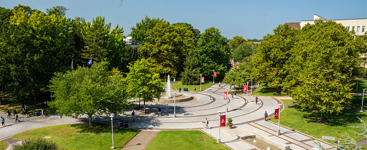 Students are scattered throughout a campus plaza near a fountain.