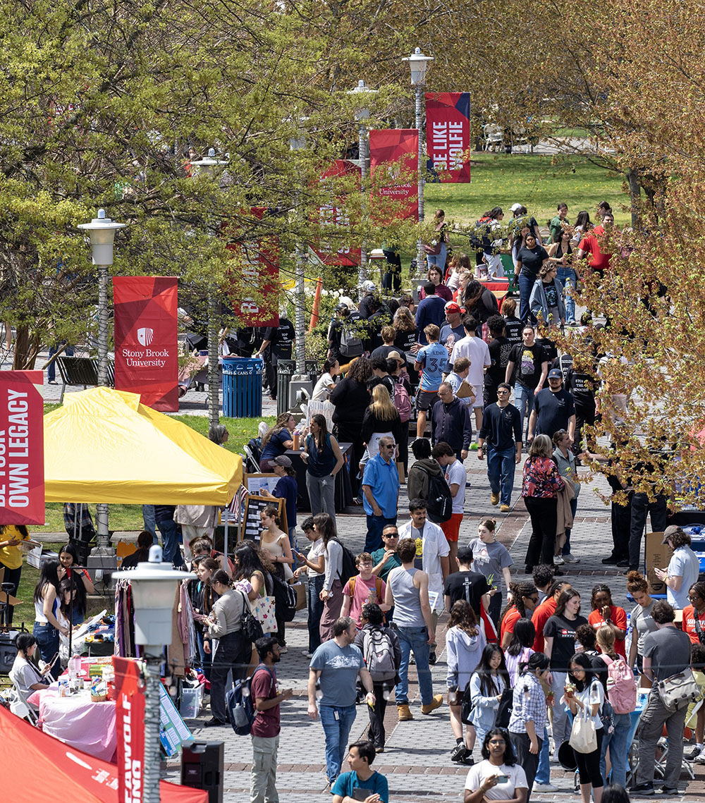Crowded campus walkway with students exploring booths and activities at an outdoor event.