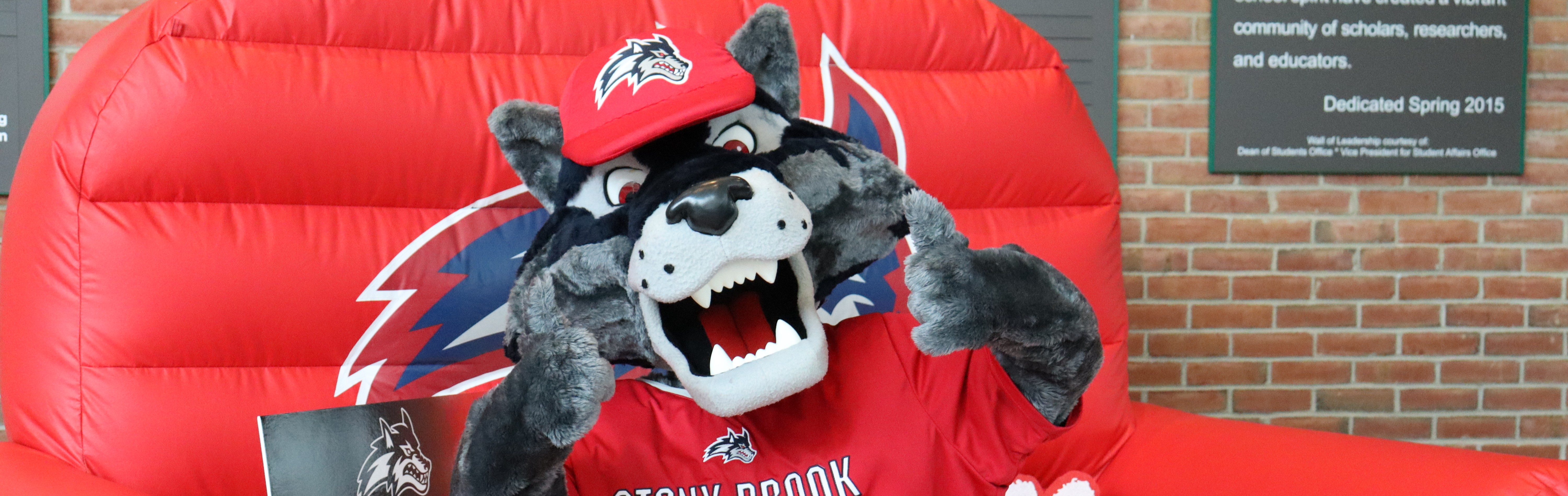 Three female sitting on a big red inflatable chair with a wolf mascot