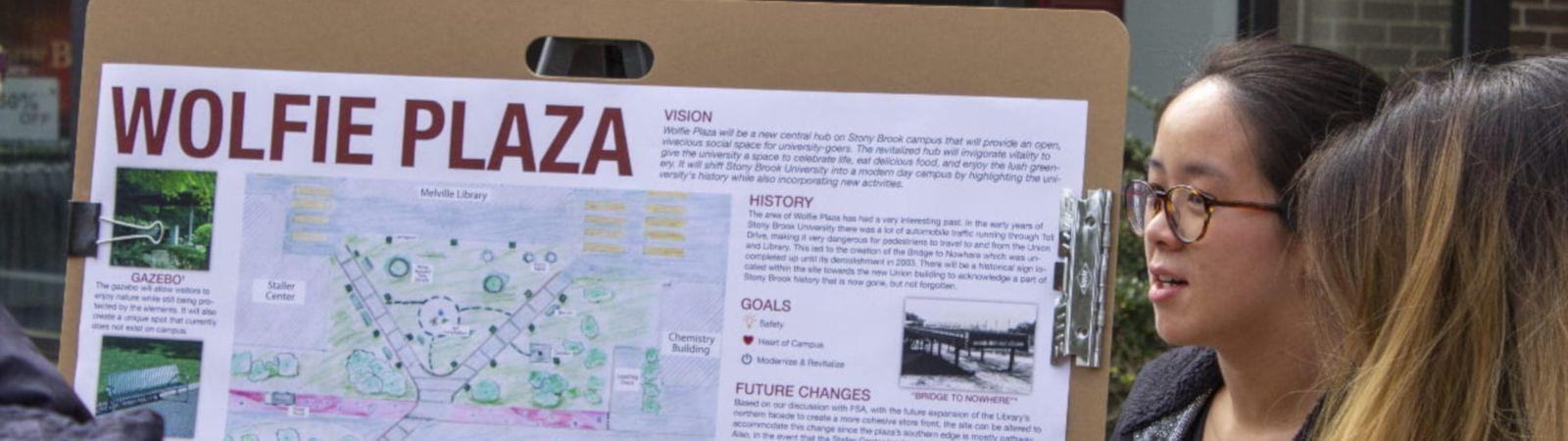 A student presents a poster that proposes a design for a Wolfie Plaza outside of the Melville Library
