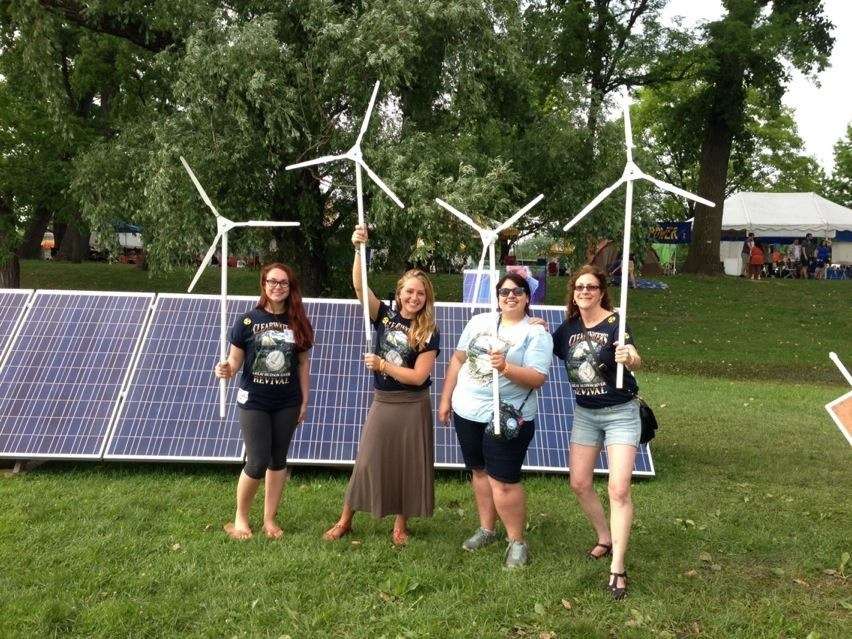 Students hold wind turbines while standing in front of a solar panel array