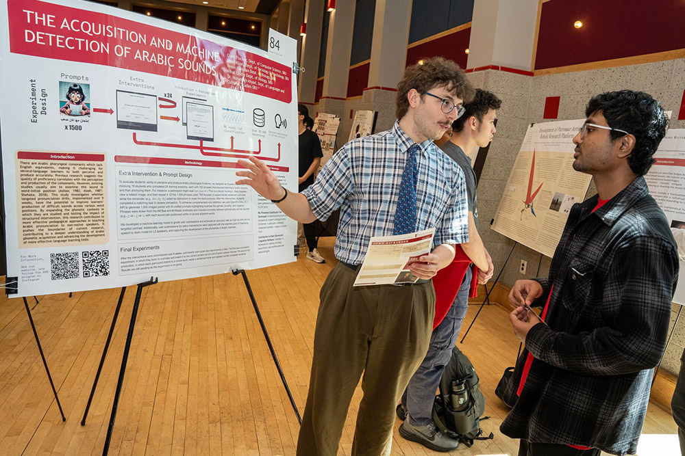 Student speaking with another student in front of a poster board.