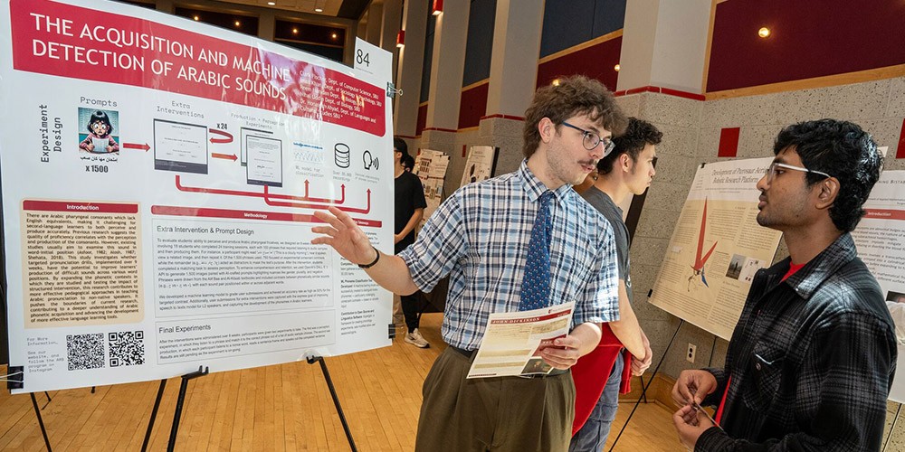 Student speaking to others in front of a research poster board.