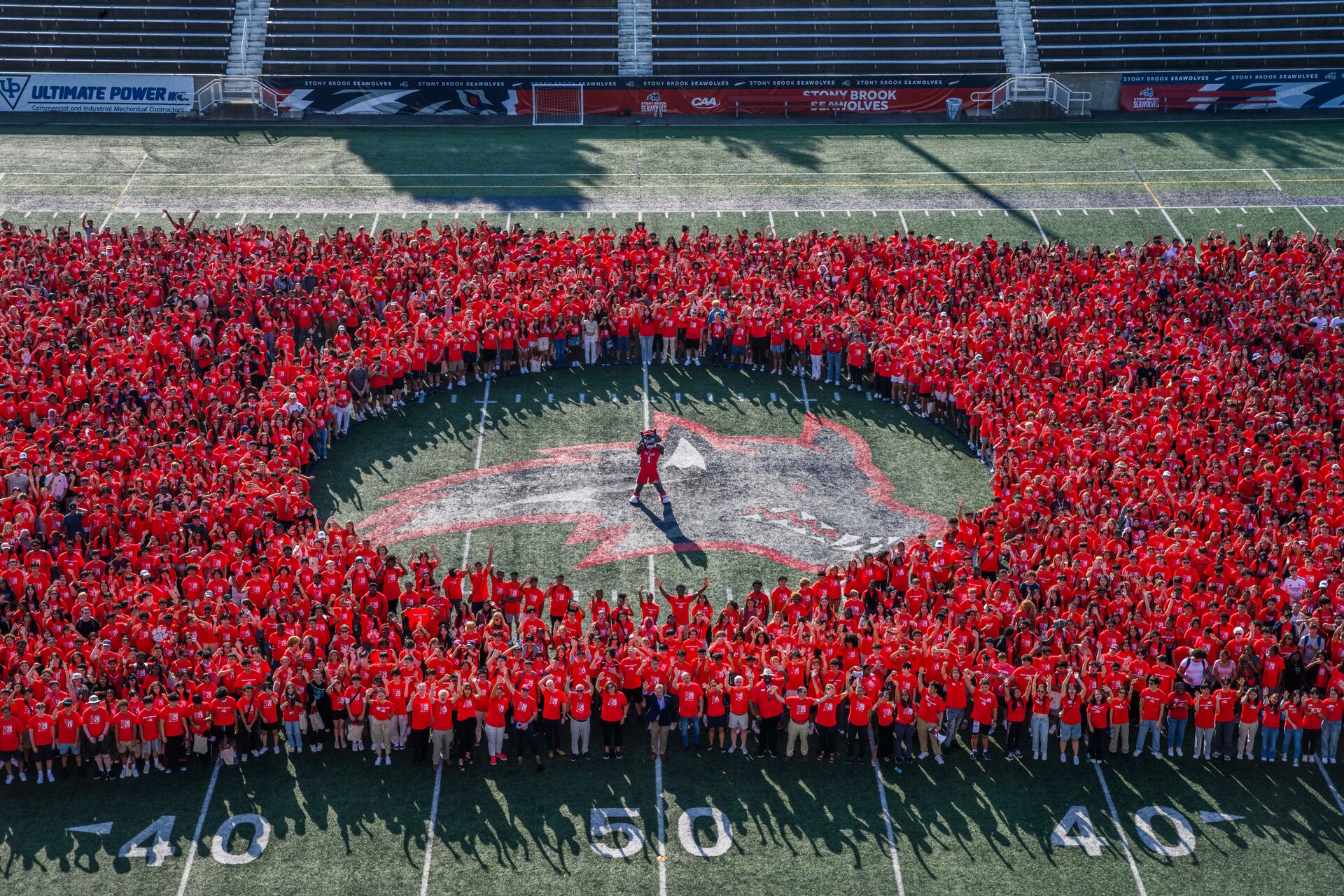 Aerial view of a large group of students posing around Wolfie on the stadium field