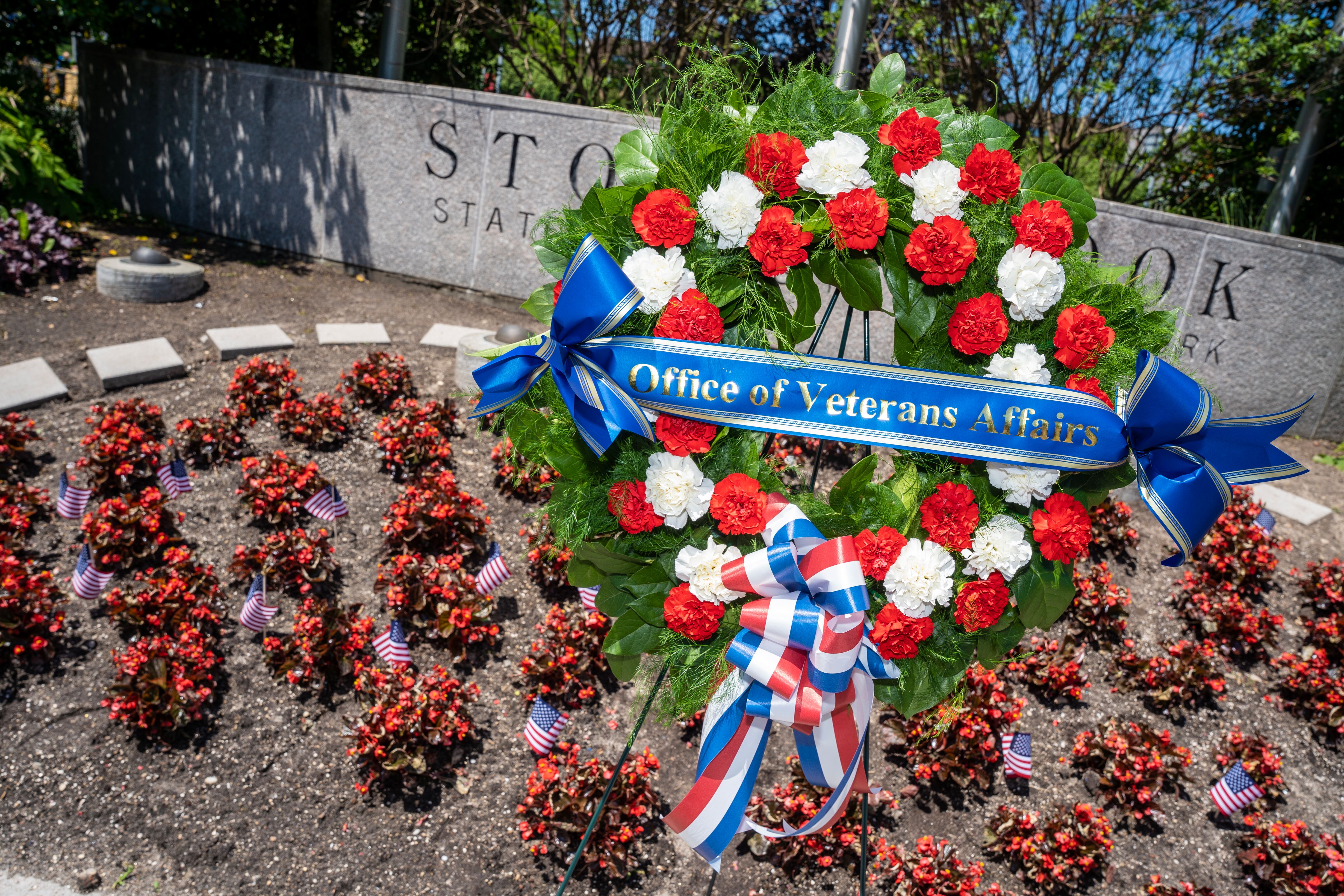 Memorial day wreath decorated with a ribbon with text "Office of Veterans Affairs" in front of the main Stony Brook University sign