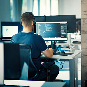 Over-the-shoulder shot of a man wearing a headset at his computer looking at code