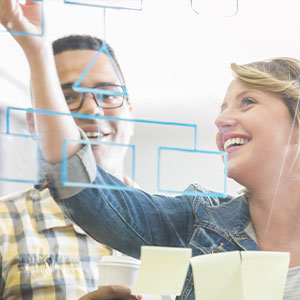 Two colleagues drawing a workflow on a transparent whiteboard.